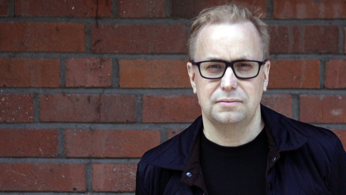 Person i svarta kläder och svarta glasögon framför en tegelvägg.