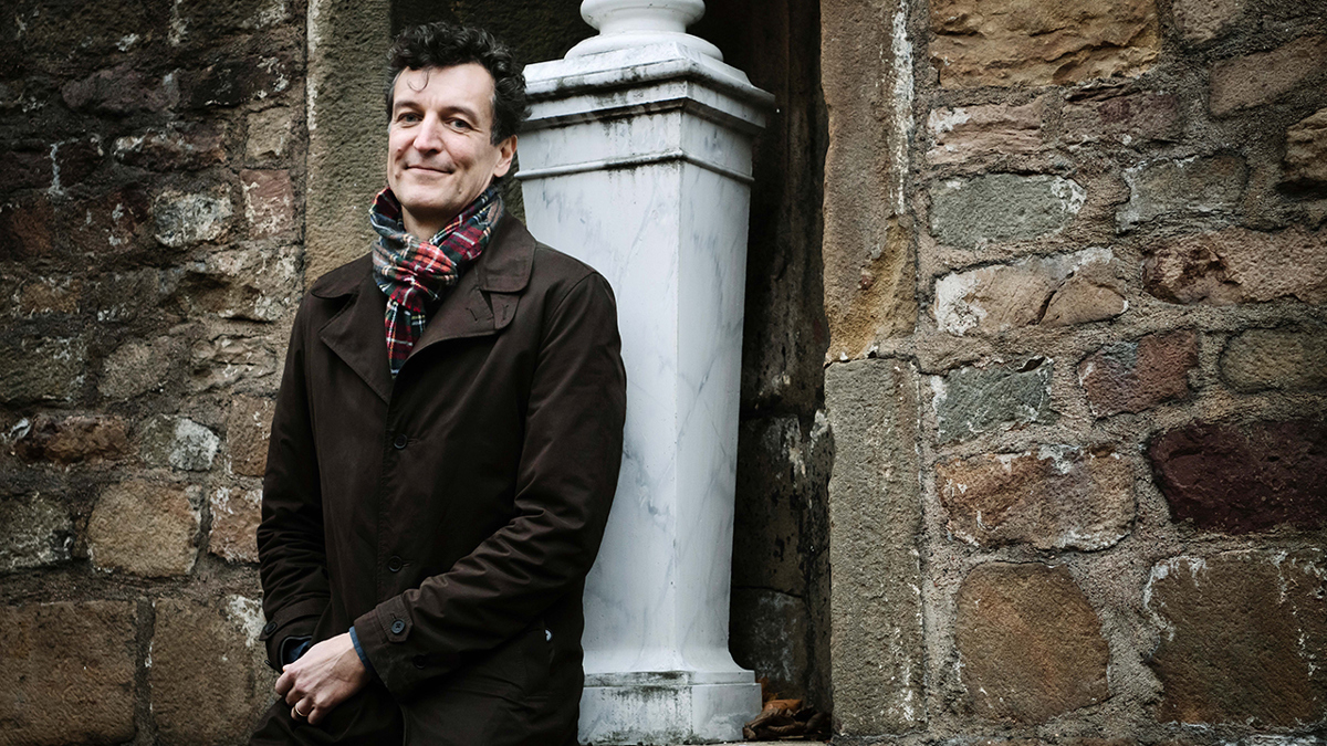 Person stående framför äldre husvägg byggd av sten.