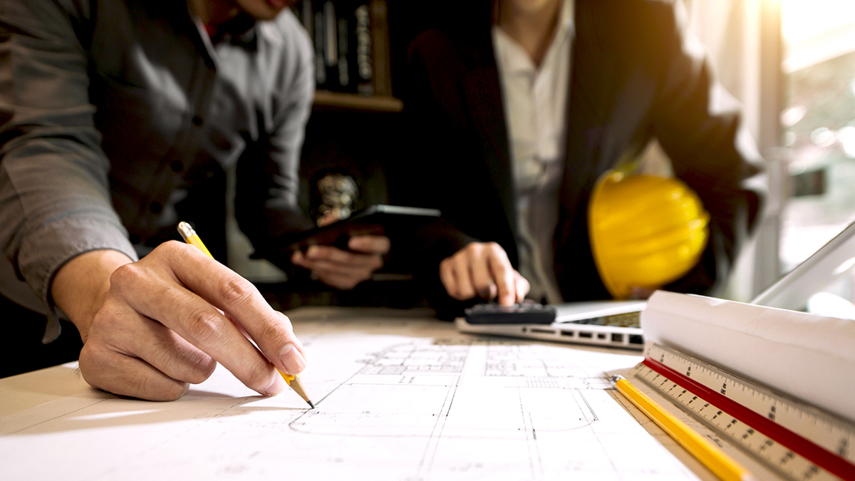 Två personer vid ett ritbord där de tillsammans diskuterar en byggplan.