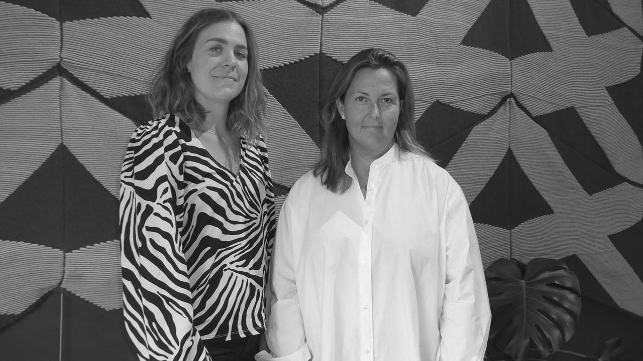 Porträtt av två personer som står framför en mönstrad vägg.