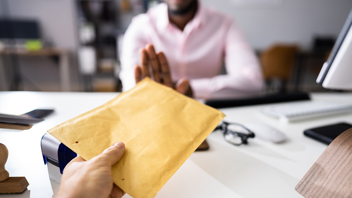 Person försöker räcka över ett kuvert med pengar till en handläggare och som gör stopptecken med högra handen.
