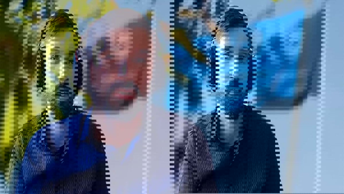 Person iförd blå skjorta och med hörlurar, mot en bakgrund som visar ett träd och Göteborgs universitets flagga.