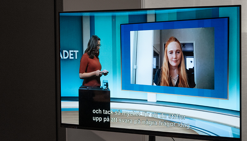 En person stående i studiomiljö intervjuar en person som deltar i sändningen via länk.