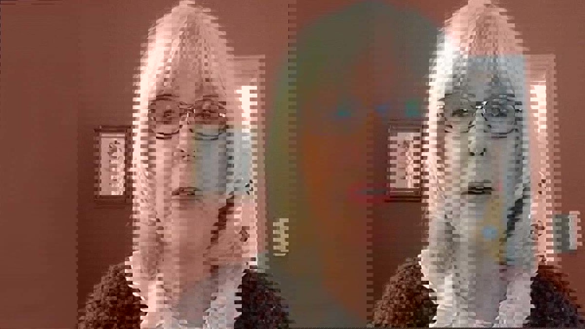 person iförd glasögon, vit blus och brun kofta.