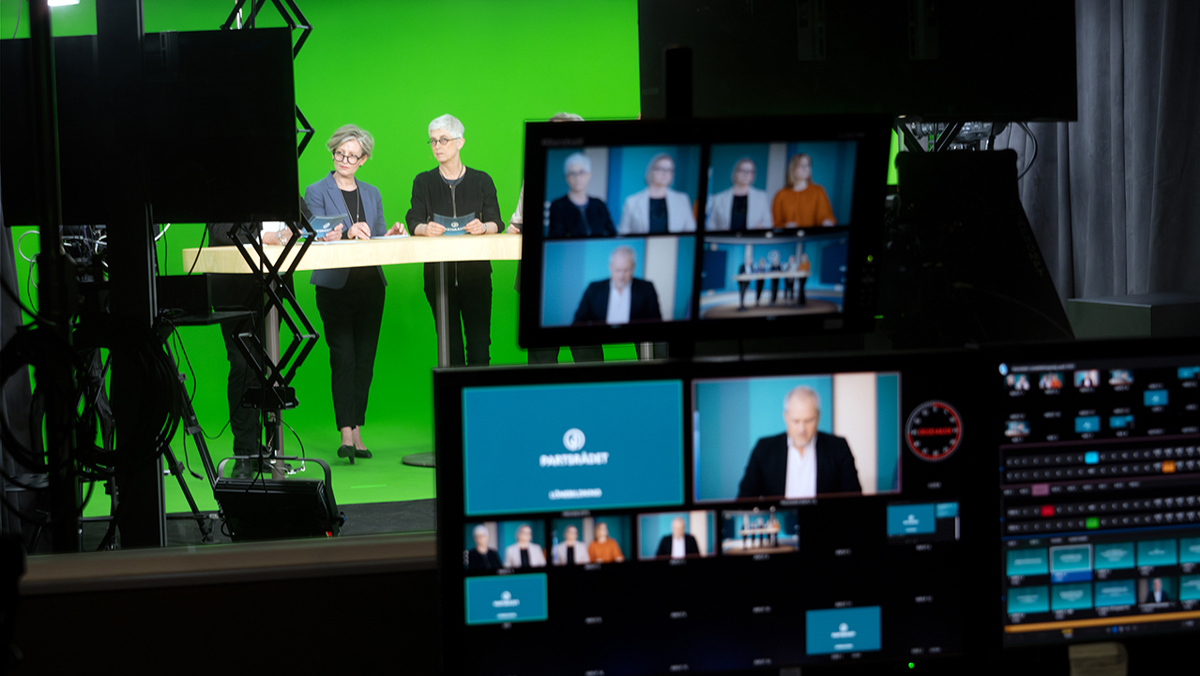 Bild tagen inne i kontrollrummet ut mot studion där centrala parters förhandlingsledningar är i direktsändning.