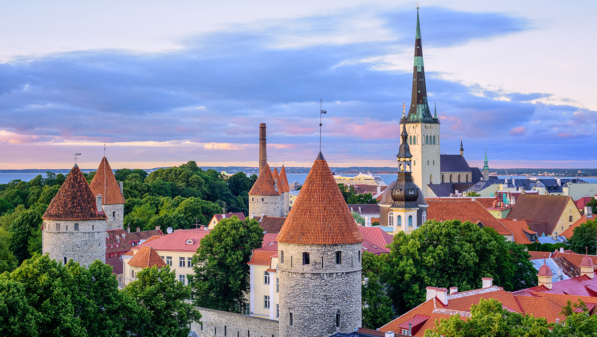 Tinnar, torn och en kyrka bland lummiga, gröna träd.