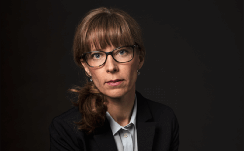 Bild på person med glasögon, svart kavaj och ljusblå blus.