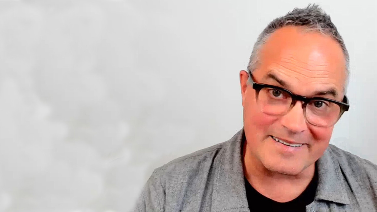 Person med glasögon och grå kavaj tittar rakt in i kameran. 