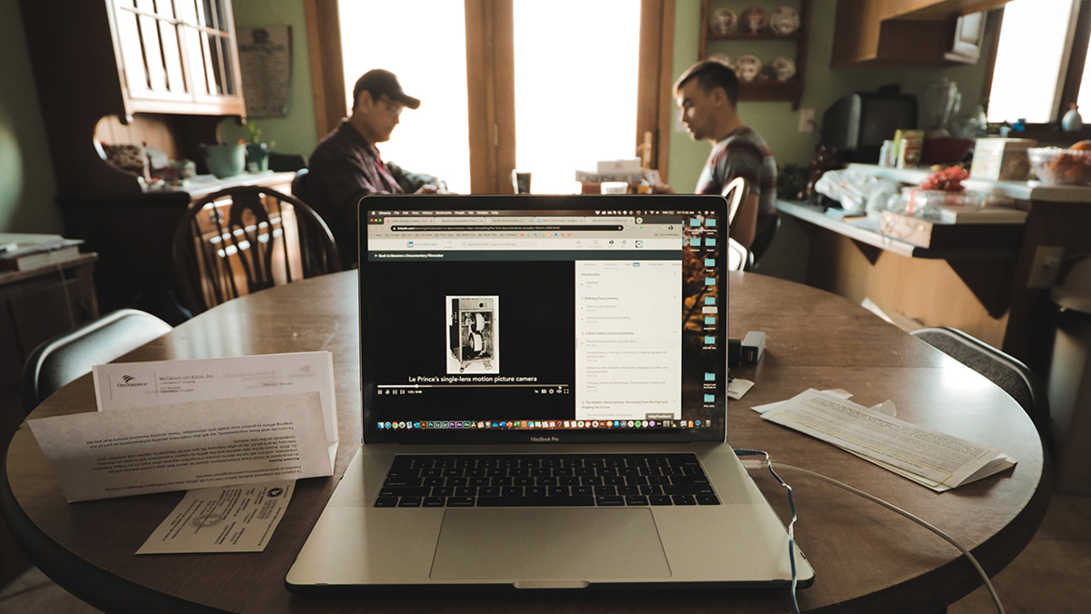 En dator på ett matbord, samt två män som sitter vid ett angränsande bord.