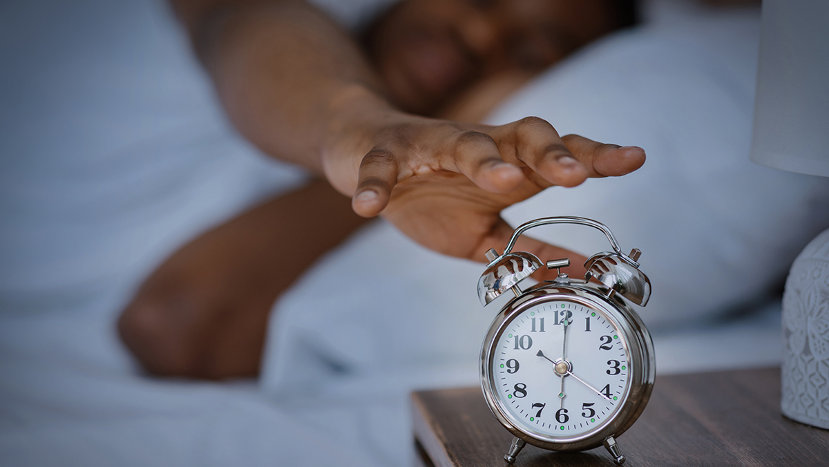 Hand som sträcker sig mot väckarklocka som står på 6.00.