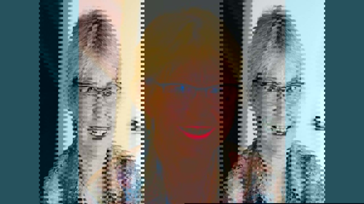 Person med ljust, kort hår, mörkbågade glasögon och flerfärgad blus.