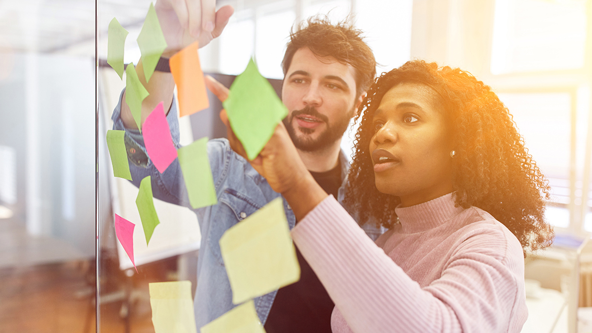 Två personer i ett mötesrum där de har satt upp notislappar på ett fönster.