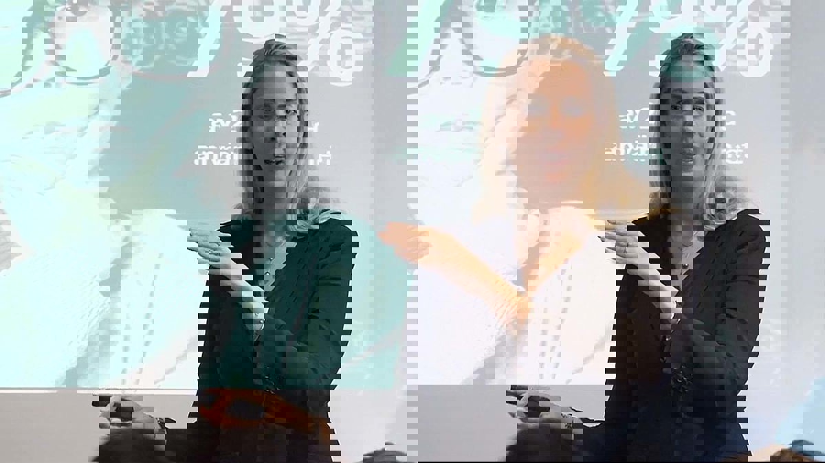 Person i seminariesituation iförd svart kavaj stående framför powertpointpresentation.