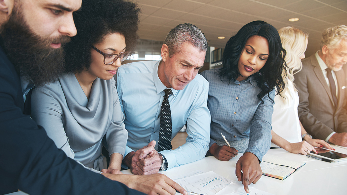 Fem personer med olik härkomst och ålder vid ett konferensbord i samtal med varandra.