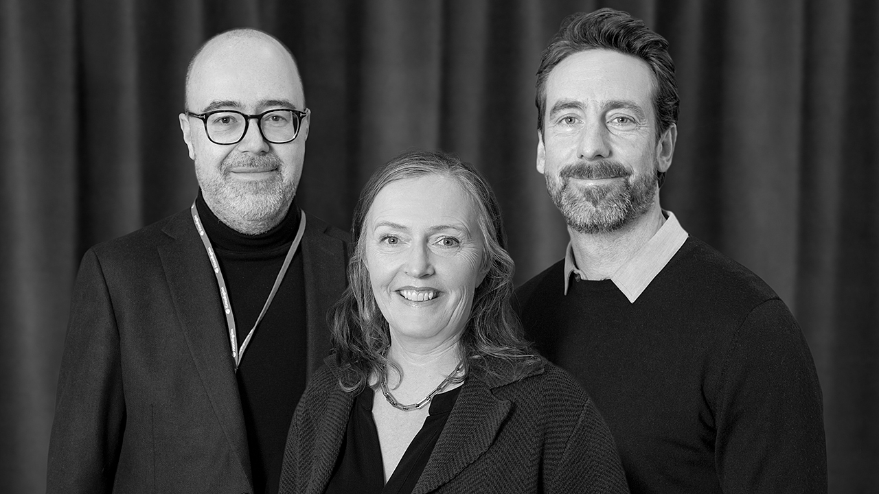 Tre personer framför ett draperi.