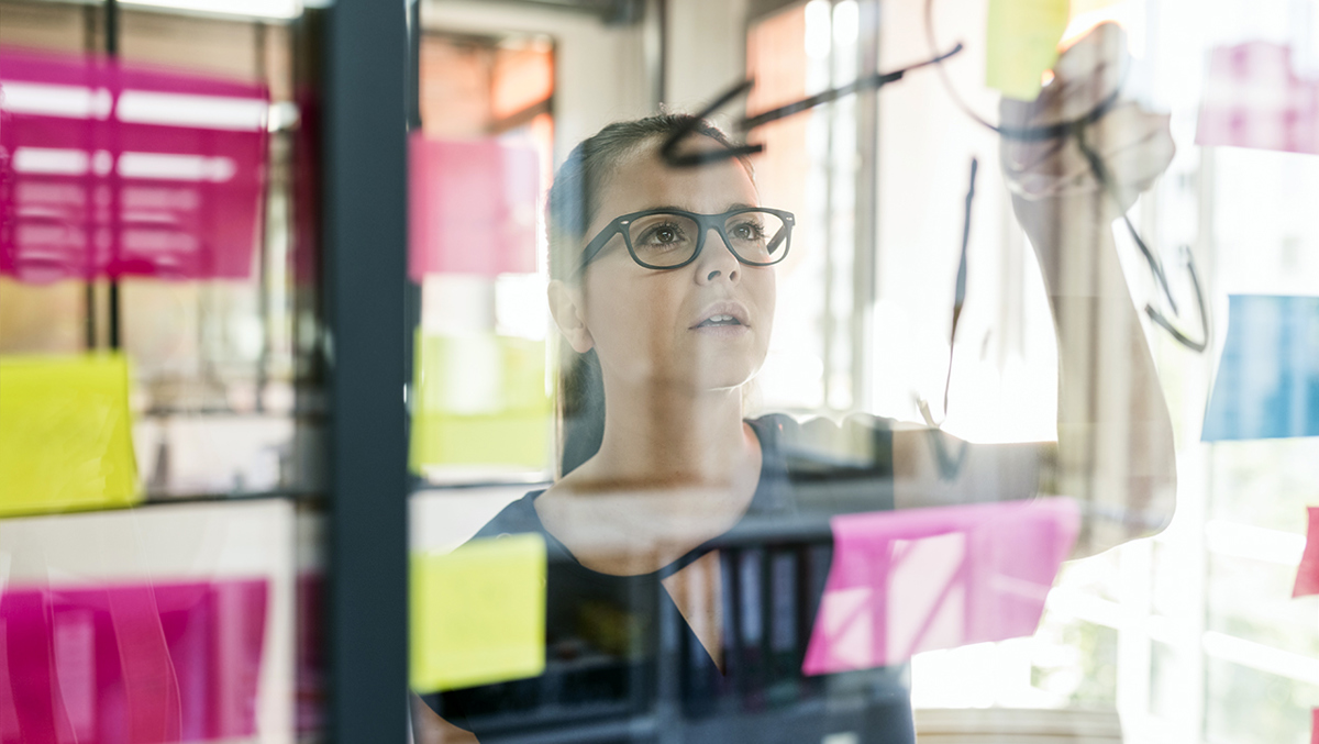Person framför glasvägg där hen läser på post-it-lappar.