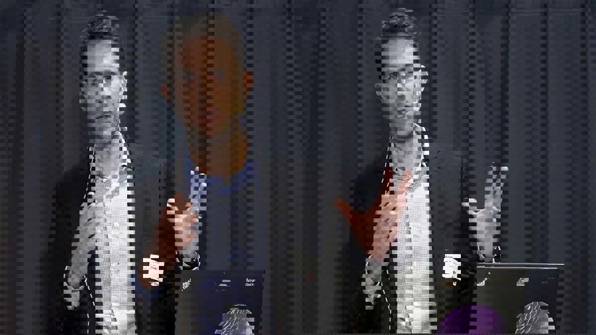 Person i seminariesituation, stående framför ett mörkt draperi.