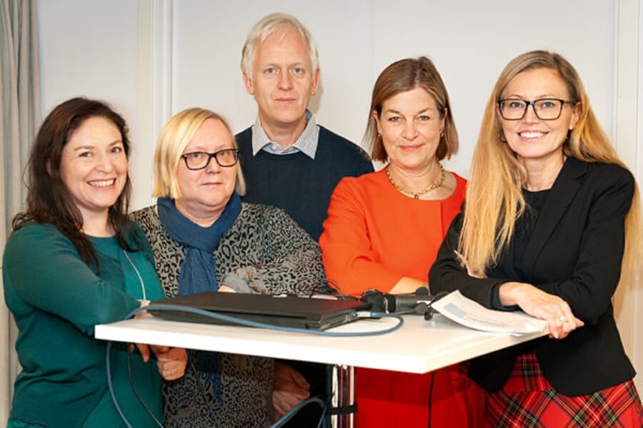 Fem personer runt ett ståbord med blicken riktad mot kameran.