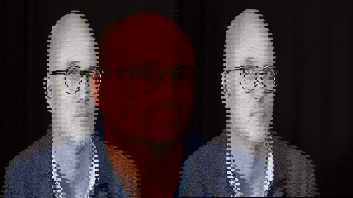 Person iförd glasögon, ljusblå skjorta och mörkblå kavaja.