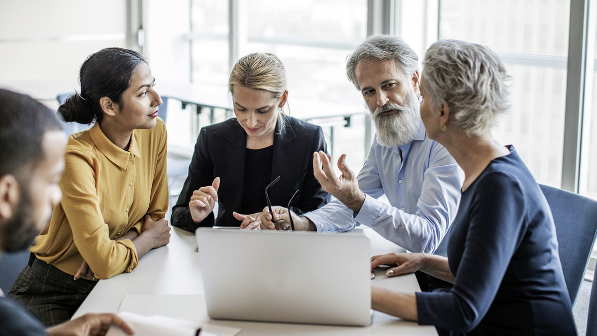 Fem personer i olika åldrar runt ett mötesbord