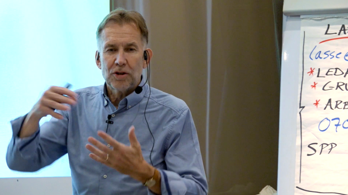 Person med mikrofonheadset framför blädderblock med text.