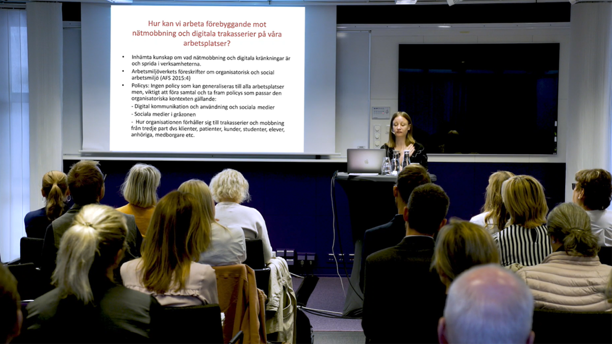 Person stående framför åhörare på ett seminarium.