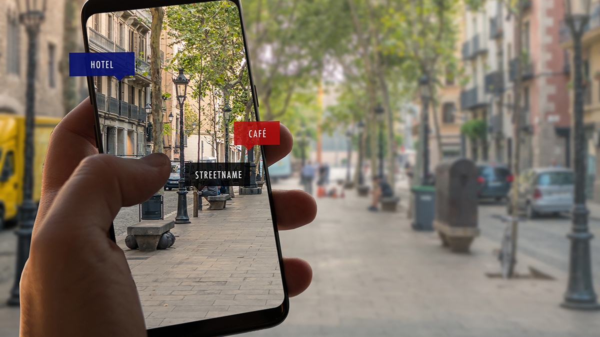 Bild på hand som håller i mobiltelefon och samtidigt tar bild på gata.