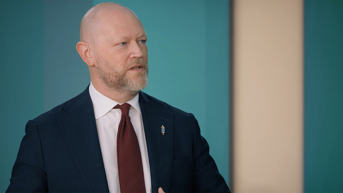 Person i studiomiljö iförd kavaj, slips och vit skjorta.