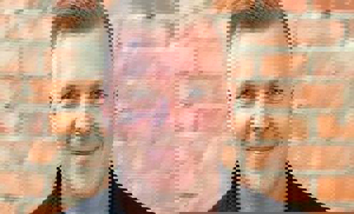 Person iförd svart skjorta stående framför tegelvägg.